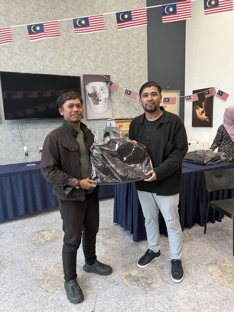Team member in a charcoal jacket receives a 3D Gens bomber jacket