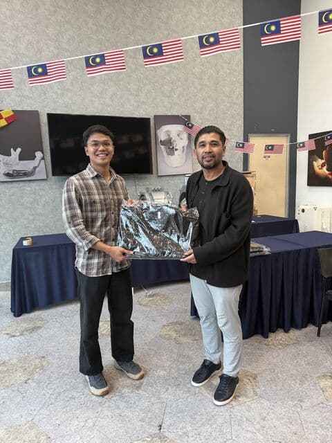 Team member in a plaid shirt receives a 3D Gens bomber jacket