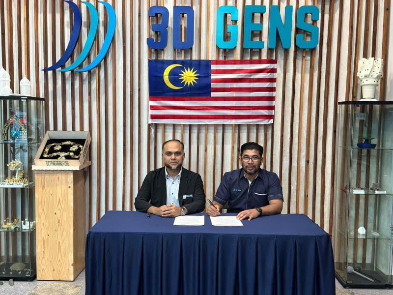 Two representatives seated together with documents in front of the 3D Gens sign